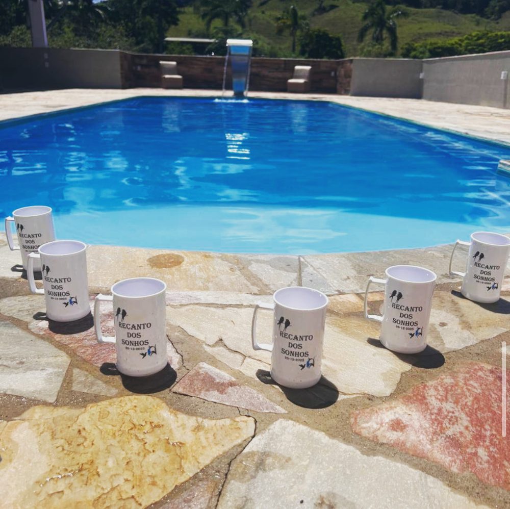 Piscina com cascata cercada por pedra, com canecas do Recanto dos Sonhos na borda